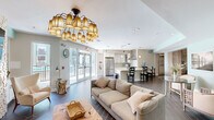 This well-appointed single-floor communal space offers a seamless open-plan layout that integrates a living lounge, a fully equipped kitchen, and a recreation area into one cohesive environment. The living area serves as the centerpiece, anchored by a striking stone-clad fireplace flanked by built-in shelving and topped with a wall-mounted television. Comfortable neutral-toned sofas, a rustic live-edge coffee table, and an elegant multi-shade chandelier create a warm, inviting ambiance. Wood-look tile flooring in a herringbone pattern runs throughout, lending both texture and continuity to the space. Adjacent to the lounge, a dedicated recreation zone features a billiards table set beneath the same statement chandelier, with soft aqua-toned accent walls adding a fresh, coastal feel. The fully equipped kitchen boasts crisp white shaker cabinetry, light quartz countertops, a subway tile backsplash, and premium stainless steel appliances including a large French door refrigerator, a gas range, and a stainless hood. A curved breakfast bar with elegant swivel barstools provides additional seating. Large glass doors open to an outdoor area, allowing abundant natural light to fill the space and offering easy access to exterior amenities.