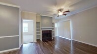 This single-story home offers a well-organized layout with a cohesive design throughout. The living area serves as a central focal point, highlighted by a dark tile-surround fireplace flanked by built-in open shelving on both sides. Crown molding lines the ceiling, and a ceiling fan adds both function and style. Rich, dark hardwood-style flooring flows through the main living spaces, complementing the neutral wall tones. Large mirrored closet doors in the living area enhance the sense of space and reflect natural light.

The kitchen is well-appointed with white cabinetry, dark stone-look countertops, a tiled mosaic backsplash, and black appliances including a range, microwave, and dishwasher. A breakfast bar provides a casual dining option and connects the kitchen to the main living area.

Bedrooms feature plush carpet flooring, ceiling fans, and generous natural light from sizable windows fitted with blinds. The bathrooms are finished consistently with white cabinetry, dark countertops, tile-surround tub-shower combinations, and hardwood-style flooring. The overall design presents a clean, functional, and cohesive aesthetic throughout the home.