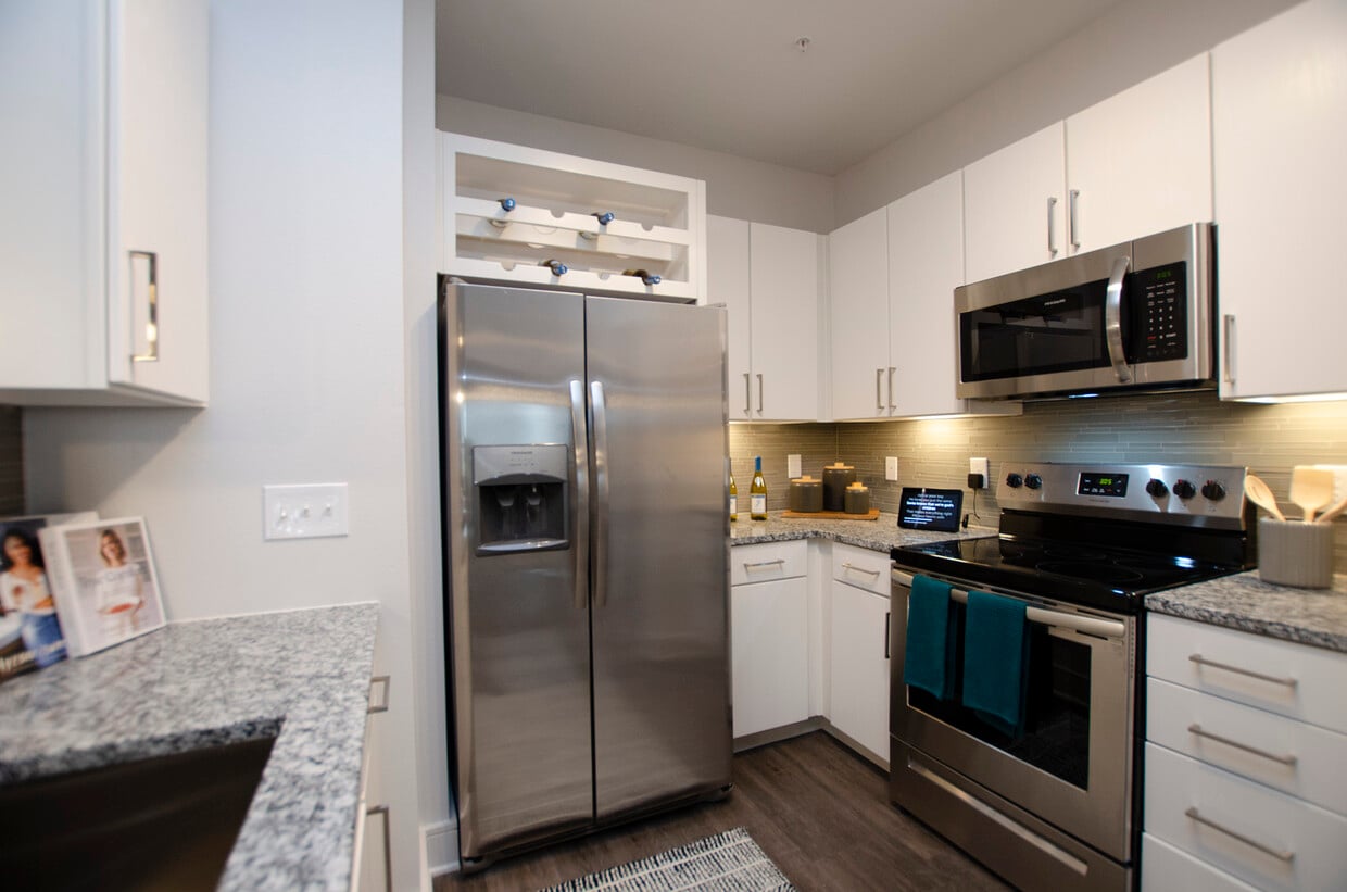 Kitchen with white cabinetry, speckled granite countertops, grey tile backsplash, stainless steel appliances, and hard surface flooring - Avalon Frisco North