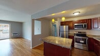 This single-floor residence offers a thoughtfully designed layout that balances functional living spaces with comfortable, understated style. The kitchen serves as a central highlight, showcasing rich cherry wood cabinetry, granite countertops with warm tonal variation, and a full suite of stainless steel appliances including a refrigerator, range, and built-in microwave. A peninsula with pendant lighting overhead provides additional prep space and a casual gathering spot, while dark tile flooring grounds the kitchen area with a bold contrast.

The open flow from the kitchen connects seamlessly into the living area, where warm hardwood flooring extends throughout. The main living space is generously sized, filled with natural light from a sliding glass door that opens to an outdoor balcony area. A ceiling fan adds both comfort and character to an additional room nearby.

The bedrooms feature the same polished hardwood floors, soft neutral walls, and multiple windows that invite natural light and outdoor views. Ample closet space is provided in the bedroom areas. The bathroom is clean and classic, finished with white subway tile surrounding a tub-shower combination, complemented by dark tile flooring and chrome fixtures. Throughout the space, a consistent cool-gray palette creates a calm, cohesive ambiance.