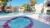 This single-story community showcases a well-appointed outdoor recreational area centered around a generously sized freeform swimming pool with striking red-trimmed coping. The pool's clear turquoise water reflects the abundant desert sunshine, creating an inviting atmosphere year-round. Adjacent to the main pool sits a circular spa/hot tub, also accented with the same distinctive red border, offering a relaxing complement to the larger swimming area.

The surrounding pool deck provides ample space for lounge chairs and outdoor furniture, making it ideal for sunbathing and leisure. A perimeter fence encloses the recreational area, ensuring privacy and security for residents and guests.

The architectural aesthetic throughout the community reflects classic Southwestern design, characterized by warm yellow stucco exteriors, terra cotta roof accents, and clean geometric forms. Mature palm trees and shade trees are thoughtfully distributed across the grounds, providing natural beauty and relief from the desert heat. Manicured shrubs and landscaping further enhance the outdoor environment. The overall ambiance is relaxed and resort-like, offering a tranquil retreat suited to warm-climate living.