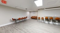 Located at 1131 University Boulevard West in Silver Spring, MD, this single-floor multipurpose space is thoughtfully designed to accommodate gatherings, events, or collaborative activities. The open-plan layout is anchored by light gray luxury vinyl plank flooring and neutral-toned walls, creating a clean and modern aesthetic throughout.

The main area features an extended bar-height counter lined with a row of cognac leather bucket chairs, offering ample seating for group events or casual meetings. A wall-mounted mini-split HVAC system ensures year-round climate comfort. Overhead, large flush-panel light fixtures provide bright, even illumination across the space.

A dedicated kitchenette at the rear is well-appointed with dark espresso cabinetry, granite countertops, stainless steel appliances including a full-size refrigerator, microwave, and dishwasher, and a distinctive mosaic tile backsplash that adds a decorative touch. An additional mini-split unit services this area independently.

A separate lounge alcove offers a more relaxed setting, furnished with a tufted cognac leather sofa, ideal for informal conversation or a quiet retreat from the main gathering area. The overall design balances functionality with comfort, making this a well-equipped and inviting venue for a variety of uses.