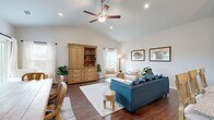 This single-story home features a thoughtfully designed open-concept layout connecting the living room, dining area, and kitchen into one cohesive, light-filled space. The living room is a standout, boasting vaulted ceilings with a ceiling fan, recessed lighting, and rich hardwood flooring. Large windows dressed with sheer white curtains invite abundant natural light, creating a warm and airy atmosphere.

The kitchen is equipped with white shaker cabinetry, stainless steel appliances, granite countertops, and a peninsula with bar seating and pendant lighting overhead. The adjacent dining area comfortably accommodates a full table and benefits from the same high ceilings that amplify the sense of space.

The primary bedroom features a ceiling fan, a window with outdoor views, and neutral tones for a calm, restful environment. Additional bedrooms are similarly bright, each with windows providing natural light. The bathrooms are finished with white vanity cabinetry and granite countertops. A dedicated laundry room with full-size washer and dryer adds everyday convenience. Two closets and a hallway complete the functional layout of this well-appointed home.