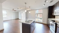 This 2-bedroom, 2-bathroom residence combines contemporary design with functional living across a single, well-organized floor. The open-concept kitchen and living area serves as the heart of the home, anchored by a striking granite-topped island with a double sink and elegant pendant lighting. Dark espresso cabinetry reaches toward the ceiling, providing ample storage, while stainless steel appliances and a classic tile backsplash complete the kitchen's polished aesthetic. Rich hardwood flooring flows throughout the main living areas, complemented by track lighting and large windows that draw in abundant natural light and frame views of the surrounding urban landscape. A dedicated hallway connects the private quarters, where both bedrooms feature plush carpeting and windows with city views. The primary bedroom offers a comfortable footprint with a walk-in closet equipped with built-in shelving. Both bathrooms are finished with granite vanity countertops, dark cabinetry, and tiled tub-shower combinations with curved curtain rods. A closet provides additional storage. Clean white walls, consistent finishes, and a cohesive design language throughout give this residence a modern, move-in-ready feel with an inviting urban ambiance.