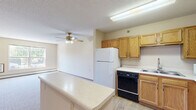 Located at 115 East Ave in Mahtomedi, MN, this 2-bedroom, 1-bathroom unit offers a straightforward single-floor layout designed for comfortable everyday living. The floor plan, as visible in the overhead view, includes a living area, kitchen, hallway, two bedrooms, and a closet, all arranged efficiently within a compact but well-utilized footprint.

The bedrooms are carpeted in neutral tones, providing a soft and quiet atmosphere. The primary bedroom is generously sized, featuring a walk-in closet with wire shelving for organized storage, and a pendant light fixture. The second bedroom includes a ceiling fan with integrated lighting, a baseboard heater, and a window that allows natural light and views of surrounding greenery. Both rooms maintain a clean, understated aesthetic with warm beige walls and classic wood-trimmed doors.

The living area is open and bright, benefiting from large windows that invite natural light and outdoor views of mature trees. A wall-mounted air conditioning unit and baseboard heating provide year-round climate control. The kitchen area, visible in the overhead layout, features wood-toned cabinetry, white appliances, and a functional workspace. Textured ceilings are consistent throughout, adding a classic residential character to the space.