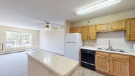 Located at 115 East Ave in Mahtomedi, MN, this 2-bedroom, 1-bathroom unit offers a straightforward single-floor layout designed for comfortable everyday living. The floor plan, as visible in the overhead view, includes a living area, kitchen, hallway, two bedrooms, and a closet, all arranged efficiently within a compact but well-utilized footprint.

The bedrooms are carpeted in neutral tones, providing a soft and quiet atmosphere. The primary bedroom is generously sized, featuring a walk-in closet with wire shelving for organized storage, and a pendant light fixture. The second bedroom includes a ceiling fan with integrated lighting, a baseboard heater, and a window that allows natural light and views of surrounding greenery. Both rooms maintain a clean, understated aesthetic with warm beige walls and classic wood-trimmed doors.

The living area is open and bright, benefiting from large windows that invite natural light and outdoor views of mature trees. A wall-mounted air conditioning unit and baseboard heating provide year-round climate control. The kitchen area, visible in the overhead layout, features wood-toned cabinetry, white appliances, and a functional workspace. Textured ceilings are consistent throughout, adding a classic residential character to the space.