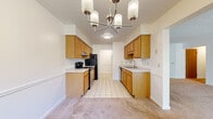 Located at 550 De George Circle in Rochester, NY, this single-floor, two-bedroom, one-bathroom residence offers a thoughtfully organized layout across a comfortable footprint. The galley-style kitchen is efficiently designed with warm oak cabinetry lining both walls, light-colored countertops, tile flooring, and black appliances including a range, refrigerator, and dishwasher. An overhead chandelier adds a decorative touch, and the kitchen flows conveniently into the adjoining hallway and dining area.

The dining room is bright and welcoming, featuring soft carpeting, a matching chandelier, chair-rail molding along the walls, and a large window that frames outdoor greenery. The living area extends toward a full-width sliding glass door that opens to an outdoor space, filling the room with natural light and views of surrounding trees.

The generously sized primary bedroom includes two closets and benefits from dual windows overlooking the outdoors, while the second bedroom offers carpeted flooring and chair-rail detailing. The full bathroom is finished with tile flooring and a tub-shower combination. Throughout the residence, neutral tones and carpet flooring create a cohesive, understated ambiance.