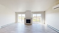 Located at 1880 E Deerfield Ave in Suamico, Wisconsin, this well-appointed single-floor home offers two bedrooms, two bathrooms, and a thoughtfully designed layout. The living room is an immediate highlight, featuring a striking central fireplace flanked by large sliding glass doors and picture windows that flood the space with natural light and frame open outdoor views of the surrounding landscape. Light-toned luxury vinyl plank flooring runs throughout, complementing the home's clean, neutral color palette.

The kitchen is outfitted with rich dark wood cabinetry, granite countertops, a central island with additional granite surface space, and a full suite of stainless steel appliances including a refrigerator, range, microwave, and dishwasher. Vaulted ceilings and a modern chandelier add dimension and elegance to the kitchen area.

The spacious primary bedroom features dual windows, a ceiling fan, and generous proportions. The second bedroom provides a comfortable, light-filled space. Both bathrooms echo the home's design consistency with granite-topped dark wood vanities and light wood-look flooring. One bathroom includes a walk-in shower, while the other features a window for added ventilation. A dedicated closet rounds out the functional layout of this inviting home.