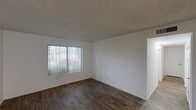 This single-story residence offers a practical and well-organized layout across three bedrooms, one bathroom, a living room, and a combined dining room and kitchen. Wood-style flooring runs throughout the home, providing a cohesive and easy-to-maintain aesthetic in every room. The living area features neutral white walls and a textured ceiling, creating a clean, versatile canvas. The kitchen is well-appointed with warm wood cabinetry, light countertops, black appliances including a refrigerator and range, a double-basin sink, and a ceiling-mounted light fixture, making it both functional and inviting. The dining area flows naturally from the kitchen. The three bedrooms each feature wood-style flooring, white walls, and windows that allow natural light to filter in. The primary bedroom is generously proportioned, with vertical blinds offering privacy and outdoor views. A second bedroom features a ceiling fan with light and lighter-toned flooring, while the third bedroom provides a compact, efficient space. Two hallways connect the rooms efficiently. The full bathroom includes a tub-shower combination with a curtain rod. Textured ceilings are present in multiple rooms, adding a classic residential touch throughout the home.