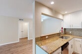Located at 1001 Pinemont Drive in Houston, TX, this single-story 1-bedroom, 1-bathroom unit offers a well-designed, efficient layout with consistent light wood flooring and neutral warm-beige walls throughout. The welcoming entrance features built-in hooks and a bench, providing practical storage right at the door. The open-concept kitchen is a standout, boasting granite countertops, a mosaic tile backsplash, white shaker cabinetry, stainless steel appliances including a range, microwave, and dishwasher, and a stainless steel sink. A pass-through counter connects the kitchen to the living and dining areas, creating an open, airy feel ideal for everyday living and entertaining. The living room is spacious and bright, bathed in natural light, with a ceiling fan overhead. The dining area flows naturally from the living space, offering room for a full dining setup. The bedroom is a comfortable size, featuring a ceiling fan, a window with natural light, and access to a closet. The bathroom is well-appointed with granite countertops, white cabinetry, wood-look flooring, and a tiled tub-shower combination with a decorative mosaic accent strip. An in-unit laundry area adds everyday convenience to this thoughtfully designed Houston home.