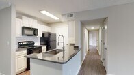 This single-floor residence is designed with a clean, functional layout that flows comfortably from room to room. The kitchen serves as a central highlight, featuring a galley-style configuration with white shaker cabinetry, gray countertops, subway tile backsplash, and black appliances including a range, refrigerator, microwave, and dishwasher. A peninsula island with an undermount sink and a sleek pull-down faucet extends into the adjoining space, offering additional prep and seating potential. Wood-look flooring runs consistently throughout the unit, lending a cohesive and low-maintenance aesthetic.

The living area is generously proportioned, with multiple windows fitted with horizontal blinds that allow ample natural light. A ceiling fan with an integrated light fixture adds both comfort and illumination. The textured ceiling is a consistent feature throughout the home.

Multiple bedrooms share a similar design language — each offering wood-look flooring, neutral wall tones, a ceiling fan, and a window with natural light. The hallway connects the bedrooms efficiently to the rest of the unit.

The bathrooms feature white vanity cabinetry, gray countertops, an undermount sink, a large mirror, and wood-look flooring, maintaining the consistent design palette found throughout the space.