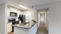 This single-floor residence is designed with a clean, functional layout that flows comfortably from room to room. The kitchen serves as a central highlight, featuring a galley-style configuration with white shaker cabinetry, gray countertops, subway tile backsplash, and black appliances including a range, refrigerator, microwave, and dishwasher. A peninsula island with an undermount sink and a sleek pull-down faucet extends into the adjoining space, offering additional prep and seating potential. Wood-look flooring runs consistently throughout the unit, lending a cohesive and low-maintenance aesthetic.

The living area is generously proportioned, with multiple windows fitted with horizontal blinds that allow ample natural light. A ceiling fan with an integrated light fixture adds both comfort and illumination. The textured ceiling is a consistent feature throughout the home.

Multiple bedrooms share a similar design language — each offering wood-look flooring, neutral wall tones, a ceiling fan, and a window with natural light. The hallway connects the bedrooms efficiently to the rest of the unit.

The bathrooms feature white vanity cabinetry, gray countertops, an undermount sink, a large mirror, and wood-look flooring, maintaining the consistent design palette found throughout the space.