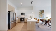 Located at 265 Terhune Road in Princeton, NJ, this thoughtfully designed one-bedroom, one-bathroom residence offers a clean, modern aesthetic throughout its single-level layout. The open-concept kitchen and living area serves as the heart of the home, anchored by a sleek kitchen featuring two-tone cabinetry — crisp white upper cabinets paired with warm wood-tone lower cabinets — and a generous quartz waterfall island with bar seating. Stainless steel appliances, including a French door refrigerator, gas range, and built-in microwave, complement the contemporary design, while a white tile backsplash and matte black fixtures add refined detail. Light hardwood flooring flows seamlessly throughout the main living area, enhancing the bright, airy atmosphere. The living room is bathed in natural light through oversized black-framed windows and offers direct access to a private balcony with outdoor views. Soaring ceilings amplify the sense of openness. The bedroom is a calm, well-proportioned retreat with warm neutral tones. The bathroom features large-format light tile flooring, a white vanity, and matte black hardware for a cohesive, modern finish. A hallway and closet complete the efficiently designed floor plan, making excellent use of every square foot.