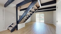 Located at 24 Rock Creek Dr in Delaware, Ohio, this two-story, 2-bedroom, 2-bathroom home offers a thoughtfully designed layout spread across two floors. The main level showcases a combined living, dining, and kitchen area that immediately draws attention with its bold, dark exposed wood ceiling beams contrasting beautifully against white walls and light hardwood-style flooring. The kitchen is equipped with stainless steel appliances — including a range, over-the-range microwave, and refrigerator — paired with crisp white cabinetry and a clean white peninsula that anchors the open-concept space. A dramatic open-riser staircase with dark wood framing serves as a striking architectural centerpiece, while a sliding glass door in the living area invites natural light and outdoor views. The main floor also includes a dedicated laundry room with washer and dryer hookups. Upstairs, two bedrooms provide comfortable retreats — one featuring the same light hardwood flooring and exposed beams, the other finished with plush carpeting and a ceiling fan. Both bathrooms are clean and functional, featuring tub-shower combinations with hardwood-style flooring. Two closets and additional storage complete this efficiently designed, characterful home.