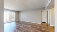 This single-floor unit offers a clean, functional layout with consistent wood-look flooring running throughout every room, providing a cohesive and easy-to-maintain aesthetic. Neutral warm-beige walls complement the light tones of the flooring, creating a bright and welcoming atmosphere across all spaces.

The living area is generously proportioned, featuring a textured ceiling, white baseboards, and a sliding glass door dressed with vertical blinds that allows natural light to pour in and provides access to an outdoor area. An adjacent room mirrors this setup with its own sliding glass door, offering flexibility as a dining space or secondary living area.

The bedrooms are well-sized, with one featuring a ceiling fan with light fixture and a window with horizontal blinds for natural ventilation and light. The wood-look flooring continues seamlessly into each bedroom, maintaining the uniform design language of the unit.

The galley-style kitchen is efficiently designed with white cabinetry, laminate countertops, white appliances including a refrigerator and range, and a dishwasher. Overhead lighting keeps the space bright and functional.

The bathroom includes a full tub and shower combination with white tile surround, chrome fixtures, and a vanity with laminate countertop and white cabinetry. The space is clean and well-appointed throughout.