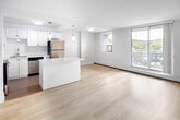 Located at 55 Tindale Court in Hamilton, Ontario, this single-floor unit presents a clean, modern aesthetic throughout. The open-concept layout connects the living area to a well-appointed kitchen, creating a seamless and functional flow. The kitchen is a standout feature, showcasing white shaker-style cabinetry extending to the ceiling, a large central island with a white quartz countertop, and a full suite of stainless steel appliances including a refrigerator, stove, built-in microwave, and dishwasher. Elegant pendant lighting hangs above the island, adding a refined touch. Light-toned tile flooring grounds the kitchen, transitioning into pale hardwood-style flooring that carries through the remainder of the unit. The living area is generously proportioned and bathed in natural light from large floor-to-ceiling windows and a sliding glass door that opens to a balcony overlooking a treed neighbourhood skyline. The bedrooms are calm and neutral in tone, each featuring light hardwood flooring, clean white trim, and ample closet space with sliding panel doors. The overall palette of soft whites and warm neutrals throughout creates a bright, cohesive, and move-in-ready living environment.