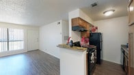 Located at 9100 Andrews Hwy in Odessa, Texas, this single-floor unit offers a practical and well-organized layout suited for comfortable everyday living. The open living area is finished with durable wood-style flooring and features a textured ceiling, clean white walls, and a sliding glass door that invites natural light and provides access to the outdoors. The space feels open and airy, with a neutral color palette that lends itself to a variety of furnishing styles.

The galley-style kitchen is efficiently designed, offering warm wood cabinetry, a black appliance suite including a range and refrigerator, an overhead ventilation hood, and a peninsula counter that connects the kitchen to the living area. Additional cabinetry and counter space runs along both sides of the kitchen, maximizing storage and functionality.

The bedrooms are carpeted for comfort and feature vertical blinds over the windows, allowing for natural light control. A ceiling fan is present in at least one bedroom, adding to the overall comfort of the space.

The bathroom is clean and functional, featuring a single vanity with a large mirror, wood-toned cabinetry below, and a neutral countertop. The layout is efficient and well-lit. Throughout the unit, consistent finishes and thoughtful design details create a cohesive, move-in ready living environment.