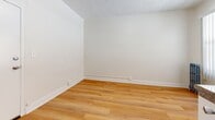 Located at 729 S Union Ave in the Westlake neighborhood of Los Angeles, this single-floor, one-bedroom, one-bathroom unit offers a efficiently designed living space. The main living area is the largest portion of the unit, featuring warm, light-toned hardwood-style flooring, crisp white walls, and a textured ceiling that adds subtle character. A window dressed with vertical blinds allows natural light to filter in while providing privacy, and a classic cast-iron radiator beneath it serves as both a functional heating element and a charming architectural detail. The kitchenette is neatly integrated into the space, outfitted with white cabinetry, a tiled backsplash, a granite-style countertop, a single-basin sink, a compact cooktop, and a mini refrigerator — providing essential kitchen functionality in a streamlined layout. The bathroom is straightforward and functional, finished in white tones with dark wood-style flooring, and includes a toilet, a walk-in shower stall, and a wall-mounted shelf. The unit's overall aesthetic is clean and minimal, making it a practical option for those seeking a no-frills living space in a central Los Angeles location.