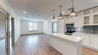 This well-designed single-floor unit offers a bright, open-concept layout that seamlessly connects the kitchen, dining, and living areas. The kitchen is a standout feature, outfitted with crisp white shaker-style cabinetry extending to the ceiling for maximum storage, a gray subway tile backsplash, a white quartz center island, and a full suite of stainless steel appliances including a French door refrigerator with ice maker, electric range, built-in microwave, and dishwasher. Brushed gold pendant lights hang above the island, adding a refined touch. The living area is spacious and filled with natural light from large windows with blinds, complemented by recessed lighting and warm wood-look flooring that runs throughout the unit. The bedrooms are generously sized, each featuring a ceiling fan, natural light from dual windows, and continued wood-look flooring. Two full bathrooms serve the unit, both featuring gray vanity cabinetry, white quartz countertops, and tile flooring. One bathroom includes a walk-in shower, while the other offers a tub-shower combination with white subway tile surround. A walk-in closet with built-in shelving and rod storage is accessible from one of the bathrooms, providing ample organization space. The clean, neutral palette and modern finishes create a cohesive and inviting atmosphere throughout.