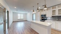 This well-designed single-floor unit offers a bright, open-concept layout that seamlessly connects the kitchen, dining, and living areas. The kitchen is a standout feature, outfitted with crisp white shaker-style cabinetry extending to the ceiling for maximum storage, a gray subway tile backsplash, a white quartz center island, and a full suite of stainless steel appliances including a French door refrigerator with ice maker, electric range, built-in microwave, and dishwasher. Brushed gold pendant lights hang above the island, adding a refined touch. The living area is spacious and filled with natural light from large windows with blinds, complemented by recessed lighting and warm wood-look flooring that runs throughout the unit. The bedrooms are generously sized, each featuring a ceiling fan, natural light from dual windows, and continued wood-look flooring. Two full bathrooms serve the unit, both featuring gray vanity cabinetry, white quartz countertops, and tile flooring. One bathroom includes a walk-in shower, while the other offers a tub-shower combination with white subway tile surround. A walk-in closet with built-in shelving and rod storage is accessible from one of the bathrooms, providing ample organization space. The clean, neutral palette and modern finishes create a cohesive and inviting atmosphere throughout.
