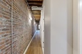 Located at 119 Hotel Street in Utica, NY, this one-bedroom, one-bathroom unit masterfully blends industrial character with contemporary design. The space is defined by its striking exposed brick walls and original wood beam ceilings, which run throughout and lend a warm, loft-like ambiance to every room.

The open-concept kitchen serves as a central highlight, featuring a large center island with a stone countertop, sleek two-tone cabinetry in white and gray, stainless steel appliances, and pendant lighting that hangs from the rustic ceiling overhead. Arched windows along the brick wall allow natural light to fill the space and offer views of the surrounding neighborhood.

A long hallway — itself an architectural feature — runs the length of the unit, its exposed brick wall, visible ductwork, and wood beam ceiling creating a dramatic industrial corridor. Light wood flooring flows consistently throughout, tying the spaces together cohesively.

The bedroom is a calm, neutral retreat with smooth gray walls and the same warm hardwood floors. The bathroom is finished to a high modern standard, showcasing hexagonal tile flooring, a glass-enclosed walk-in shower with white subway tile, a dark navy vanity with marble countertop, and crisp white walls. A utility room, closet, and additional hallway spaces round out the functional layout of this thoughtfully designed unit.