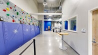 Located at 3525 Rockwood Rd in Newark, Delaware, this single-floor fitness and recreation facility offers a comprehensive range of athletic and wellness amenities across a generously proportioned footprint. The facility is designed with a clean, modern aesthetic throughout, characterized by crisp white walls accented by bold blue padding and trim, polished concrete and hardwood flooring, and bright overhead lighting supported by exposed ductwork and industrial-style ceilings that lend an open, energetic atmosphere.

The centerpiece of the facility is a large multi-sport indoor court featuring clearly marked lines for basketball and volleyball, complete with wall-mounted backboards and a portable net. Blue padded wall protectors line the perimeter, ensuring safety during play. High clerestory windows allow natural light to filter in, enhancing the airy feel of the space.

The exercise room is expansive, housing a wide array of strength training machines, free weights, and cardio equipment including treadmills and stationary bikes. Large windows bring in natural light and outdoor views, while mirrored walls add depth to the space.

Additional areas include a flexible studio room with hardwood flooring and generous natural light—ideal for group classes or personal training—and an open lobby entrance featuring a colorful rock climbing wall, a reception window, and ample circulation space. A bathroom rounds out the facility's functional amenities.