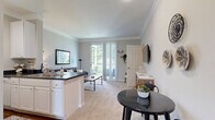 This one-bedroom, one-bathroom residence in Columbus, Ohio offers a thoughtfully designed single-floor layout that maximizes every square foot. The open-concept living and dining area is bright and welcoming, featuring crown molding, soft neutral tones, and plush carpeting. A sliding glass door floods the space with natural light and provides direct access to a private patio, offering pleasant outdoor views. The kitchen is designed in a classic galley style, outfitted with white cabinetry, dark countertops, a full suite of white appliances, and wood-look flooring that adds warmth and contrast. A dedicated dining area adjacent to the kitchen provides a comfortable space for meals. The bedroom is generously sized, featuring dual windows that bring in abundant natural light, soft carpet underfoot, and ample closet storage — with three closets found throughout the unit. The full bathroom includes a tub-shower combination, a white vanity with dark countertop, and wood-look flooring that echoes the kitchen's aesthetic. A dedicated in-unit laundry room with full-sized washer and dryer hookups adds everyday convenience. A utility room and hallway complete the functional layout of this well-rounded residence.
