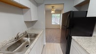 This two-story loft-style residence offers three bedrooms and two and a half bathrooms across a thoughtfully laid-out floor plan. The galley-style kitchen features white cabinetry, granite-look countertops, a stainless steel sink, and black appliances including a refrigerator and range, with light wood-look flooring underfoot and a skylight adding brightness overhead.

The main living area is generously sized, with plush carpeting, a ceiling fan, and multiple windows that invite natural light. A sliding glass door provides direct access to an outdoor area with views of surrounding greenery, enhancing the sense of openness.

The bedrooms are carpeted and finished in neutral tones, each with windows for natural light. Closets with full-width bifold doors offer practical storage. The two full bathrooms each include a tub-shower combination with tiled surrounds — one features a dark-stained vanity with a white countertop and wood-look tile flooring. The half bathroom offers a matching dark vanity and is conveniently sized for guests.

Throughout the space, a consistent neutral color palette and clean finishes contribute to a calm, functional ambiance suited for comfortable everyday living.