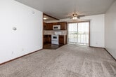 Located at 1165 Office Park Rd in West Des Moines, Iowa, this efficiently designed single-floor unit offers a practical and comfortable layout across its one-bedroom, one-bathroom floor plan. The open living area features neutral wall-to-wall carpeting, white walls, and a textured ceiling with a ceiling fan, creating a bright and functional space. A sliding glass door with vertical blinds brings in natural light and provides views of the surrounding outdoor scenery. The kitchen is open to the living area and is equipped with rich dark wood cabinetry, a classic white subway tile backsplash, wood-look flooring, and white appliances including a refrigerator, electric range, and over-the-range microwave. A built-in sink and ample counter space complete the kitchen's practical layout. An exposed wood beam accent adds a subtle architectural detail overhead. The bedroom offers generous wall space, wall-to-wall carpeting, a ceiling light fixture, and a closet for storage. The bathroom includes a single-sink vanity with dark wood cabinetry, wood-look flooring, a toilet, and a tub/shower combination. Throughout the unit, warm wood trim and door accents provide a cohesive, classic finish.