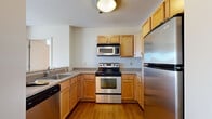 Located at 1200 Elm St in Manchester, NH, this two-bedroom, three-bathroom residence offers a well-organized single-floor layout designed for functional everyday living. The open kitchen is equipped with stainless steel appliances, including an electric range, over-the-range microwave, dishwasher, and refrigerator, complemented by warm honey-toned cabinetry, granite-style countertops, and a peninsula that provides a natural transition into the living area. The living room is bright and airy, featuring large sliding glass doors dressed with vertical blinds that frame views of the surrounding Manchester cityscape and invite generous natural light throughout the day. Hardwood-style flooring runs through the main living areas, while plush carpeting adds comfort to the bedrooms. The primary bedroom is a well-proportioned retreat with direct access to one of the three bathrooms, which includes a soaking tub, wood-style flooring, a vanity with granite-style countertops, and a lighted mirror. Additional bathrooms share similar finishes, maintaining a cohesive aesthetic throughout. Two closets provide practical storage solutions. The overall ambiance is clean, neutral, and move-in ready.