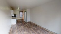 Located at 714 7th Avenue in Seattle's First Hill neighborhood, this single-floor unit offers a clean, functional layout with consistent wood-style flooring throughout. The open living area is bright and simply appointed, with neutral white walls and generous floor space that allows for flexible furniture arrangements. A window provides natural light and frames views of the surrounding urban cityscape.

The kitchen is efficiently designed with white cabinetry extending to the ceiling for ample storage, a laminate countertop with a peninsula-style breakfast bar, a double-basin sink, an electric range, a stainless steel refrigerator, a dishwasher, and a built-in microwave. The layout keeps everything accessible and well-organized.

A standout feature of the bathroom is the classic clawfoot soaking tub, fitted with a handheld shower attachment and surrounded by a ceiling-mounted oval curtain rod. The bathroom also includes a vanity with a matching laminate countertop, a wall mirror with overhead lighting, and wood-style flooring that ties the space together cohesively.

The bedroom benefits from a large sliding window that looks out onto the Seattle skyline, filling the room with natural light while offering an engaging urban view. The overall aesthetic is clean and practical, making this a well-appointed urban space in the heart of Seattle.