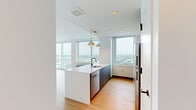 Unit 1610 at 930 Mac is a thoughtfully designed one-bedroom, one-bathroom residence that blends contemporary aesthetics with functional living. The open-concept living and kitchen area is a standout feature, anchored by expansive floor-to-ceiling windows that wrap around the space and frame sweeping panoramic city views, flooding the interior with natural light. Warm-toned hardwood flooring runs consistently throughout, complementing the clean white walls and modern finishes.

The kitchen is well-appointed with warm wood cabinetry, sleek slate-toned lower cabinets, a bold blue tile backsplash, and a suite of stainless steel appliances including a full-size refrigerator, electric range, and microwave. A generous peninsula with a white countertop and integrated sink offers additional prep space and casual seating, finished with stylish pendant lighting overhead.

The bedroom is a comfortable, well-lit retreat with its own large window overlooking the cityscape and an in-unit climate control unit. A dedicated closet provides convenient storage. The bathroom features a soaking tub and shower combination accented by striking dark blue subway tile. A hallway connects all rooms efficiently, maintaining a clean and organized flow throughout the residence.