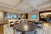 Located at 2303 Mid Ln in Houston's upscale River Oaks corridor, this elegantly designed single-floor amenity space offers a seamless blend of refined aesthetics and functional communal living. The focal point of the space is a dramatic circular bar lounge, crowned by a stunning coffered rotunda ceiling with a tiered chandelier and encircled by a curved bar top with upholstered seating. Botanical mural wallcoverings and rich dark wood millwork with brass accents lend warmth and character throughout.

A dedicated library area exudes sophistication, featuring a linear fireplace flanked by custom built-in shelving in a deep slate finish, an antler chandelier, and plush seating arranged for intimate conversation. An adjacent coffee and refreshment station is outfitted with dark wood cabinetry framed in brass, completing the lounge experience.

The dining and kitchen area is equally impressive, centered around a long marble-topped island with white upholstered barstools. Patterned encaustic tile flooring adds visual interest underfoot, while large black-framed glass doors open directly to an outdoor courtyard, flooding the space with natural light and offering views of a landscaped terrace. Wall-mounted displays and mirrored tile backsplashes enhance the sense of depth and openness throughout.