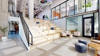 Located at 21st Street in Denver's thriving River North Art District, this two-floor commercial space blends industrial architecture with refined, contemporary design. The ground floor makes an immediate impression with soaring ceilings, exposed concrete columns, and a striking tiered staircase crafted from light wood — doubling as an amphitheater-style communal gathering area with built-in seating and small accent tables. Adjacent lounge areas feature plush, curved chairs arranged beneath a sculptural ring chandelier, while glass-partitioned rooms provide versatile private or collaborative spaces. A well-appointed café-style service counter anchors one section of the floor, complete with terrazzo flooring, a warm wood display case, and pendant globe lighting. Polished concrete floors and exposed ductwork throughout maintain an industrial character balanced by warm furnishings. The second floor opens into a bright, airy lounge bathed in natural light from expansive floor-to-ceiling windows overlooking the Denver skyline. Bold orange and yellow upholstered seating, terrazzo tile floors, and clean-lined furniture create an energetic yet comfortable atmosphere. Glass-fronted private offices and conference rooms line the corridors, offering transparency and connectivity throughout. The overall ambiance is one of modern, creative professionalism.