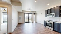 Located at 2601 Alcott St in Denver's LoHi neighborhood, this modern 2-bedroom, 1-bathroom residence offers a thoughtfully designed open-concept layout with elevated city views. The combined kitchen and living area serves as the heart of the home, featuring rich hardwood-style flooring, recessed lighting, and a ceiling fan. Floor-to-ceiling sliding glass doors open to a private balcony, flooding the space with natural light and framing sweeping views of the Denver skyline. The kitchen is outfitted with bold navy cabinetry with gold hardware, a marble-style tile backsplash, stainless steel appliances including a range, microwave, dishwasher, and refrigerator, and a stacked in-unit washer and dryer. The primary bedroom is carpeted and features a large picture window with panoramic city views and a ceiling fan, while the second bedroom also offers plush carpet and a well-sized closet. The bathroom is finished with navy vanity cabinetry, gold fixtures, a large mirror with modern lighting, and light tile flooring. A hallway connects all rooms efficiently, completing this clean, contemporary residence.