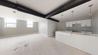 This single-floor, one-bedroom, one-bathroom unit offers a thoughtfully designed open-concept layout that maximizes its well-proportioned footprint. The living and kitchen area is immediately eye-catching, featuring bold exposed black ductwork that runs across the ceiling, lending an industrial-modern aesthetic to the space. The kitchen is equipped with white shaker-style cabinetry accented by matte black hardware, granite countertops, and pendant lighting, creating a sleek and functional workspace that flows seamlessly into the open living area. Natural light filters in through windows, brightening the neutral gray walls and light-toned flooring throughout. The generously sized primary bedroom is a standout feature, offering ample room for furnishings, dual windows that invite natural light, and a ceiling fan for added comfort. A dedicated walk-in closet with built-in wire shelving provides excellent storage capacity. The bathroom is finished with large-format tile flooring, white vanity cabinetry with granite countertops, and matte black fixtures and hardware that echo the design language found throughout the unit. Clean lines, a consistent neutral color palette, and modern finishes give the entire space a cohesive and contemporary feel.