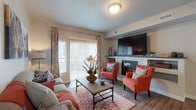 This thoughtfully designed single-floor residence offers a welcoming and cohesive living experience across all of its key spaces. The living room serves as the heart of the home, highlighted by a tiled fireplace with built-in shelving and a mounted flat-screen TV above. Warm wood-look flooring runs throughout the main living areas, complementing neutral walls and large sliding glass doors that invite natural light and provide access to an outdoor area. The kitchen is well-equipped with white shaker-style cabinetry, granite countertops, stainless steel appliances including a refrigerator, range, and microwave, and ample counter space for everyday use. Adjacent to the kitchen, the dining area features a pendant chandelier and hardwood-style flooring, creating an inviting space for shared meals. The bedrooms are carpeted for comfort, each offering generous space, natural window light, and a calm, restful ambiance. The bathroom is clean and functional, featuring a tub-shower combination with tile surround, wood-look flooring, white cabinetry, and granite countertops that carry the design language found throughout the rest of the home. Together, these spaces create a balanced and functional residence with a warm, modern aesthetic.