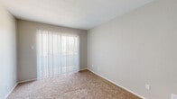 This single-story unit offers a straightforward, functional layout across several well-defined areas. The living area is spacious, finished with neutral-toned carpet and neutral gray walls, and features a sliding glass door dressed with vertical blinds that allows natural light to fill the space while providing outdoor views. A front entry door opens directly into this main living area, creating a welcoming and accessible flow throughout.

Adjacent to the living space, the kitchen is equipped with white cabinetry featuring raised-panel detailing, a granite-style laminate countertop, a double-basin sink, a white electric coil range with overhead ventilation, and a full-size refrigerator. Light wood-look flooring grounds the kitchen area, and an electrical panel is conveniently located within the kitchen space.

The bedrooms are carpeted and finished with the same neutral palette found throughout the unit. One bedroom includes a ceiling fan with a light fixture, a window with horizontal blinds, and ample wall space. Another room features a sliding glass door with vertical blinds, mirroring the living area's access to natural light.

The bathroom includes wood-look flooring, a white subway-tiled shower surround, and standard fixtures, providing a clean and classic finish. Overall, the unit presents a cohesive, neutral aesthetic throughout.