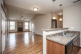This single-floor residence offers a thoughtfully designed open-concept layout that seamlessly connects the living, dining, and kitchen areas. The spacious living room is a standout, featuring vaulted ceilings, gleaming hardwood floors, a ceiling fan, and a tiled fireplace flanked by two windows that fill the space with natural light. A sliding glass door provides access to a private balcony, enhancing the sense of openness.

The kitchen is both functional and stylish, equipped with dark wood cabinetry, granite-style countertops, a double-basin sink, and black appliances including a gas range and built-in microwave. A raised breakfast bar with pendant lighting serves as a natural divider between the kitchen and the main living area, while a large pantry closet adds convenient storage.

The bedrooms are carpeted for comfort and include ceiling fans and ample natural light. The primary bedroom features a sliding door leading to a private balcony, while a secondary bedroom offers a bright window and generous closet space.

Two full bathrooms complete the unit, each finished with tile flooring, rich wood vanities, and light countertops. One bathroom includes a shower-tub combination, while the other connects directly to a bedroom. Throughout the home, warm-toned hardwood floors, vaulted ceilings, and consistent dark wood trim details contribute to a cohesive and welcoming aesthetic.