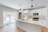 Located at 98 Old Gonic Road in Rochester, NH, this well-appointed three-bedroom, three-bathroom home is spread across three floors, offering a thoughtful layout with ample living space. The ground level includes an attached garage with an automatic opener, providing convenient and secure parking. The main living floor serves as the heart of the home, centering around a bright, open-concept kitchen and living area. The kitchen is a standout feature, showcasing crisp white shaker cabinetry, light granite countertops, a large center island with an integrated sink, stainless steel appliances including a gas range, microwave, and French door refrigerator, and dual pendant lights that add a modern touch. Sliding glass doors lead to an outdoor deck, allowing natural light to fill the space and offering views of the surrounding landscape. Hardwood-style flooring flows throughout the main and upper levels, complementing the neutral, light-toned walls. The upper floor houses the bedrooms, including a well-sized primary bedroom, along with additional bedrooms that offer bright, clean finishes. The three bathrooms are finished with tile flooring, granite-topped vanities, and tub-shower combinations with white subway tile surrounds. A closet and hallway provide additional storage and connectivity throughout the home.