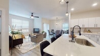 This well-appointed single-floor residence offers a bright, open-concept layout that seamlessly connects the living, dining, and kitchen areas, creating a spacious and inviting atmosphere throughout. Light-toned luxury vinyl plank flooring flows consistently across the main living spaces, complementing the neutral color palette and maximizing the sense of openness.

The kitchen is outfitted with crisp white cabinetry featuring matte black hardware, stainless steel appliances, and a striking quartz waterfall island with seating — ideal for casual dining or entertaining. Pendant lighting above the island adds a refined touch. The adjacent dining area is bathed in natural light from large sliding glass doors and features an elegant chandelier overhead. The living area is anchored by a ceiling fan and recessed lighting, enhancing comfort and functionality.

The primary bedroom provides a serene retreat with a wall-mounted mini-split system, generous natural light from a large window, and direct access to a bathroom with a tub-shower combination. A secondary bedroom offers closet space and a calm, neutral aesthetic. A dedicated laundry room houses a full-sized washer and dryer. Throughout, the residence maintains a clean, modern character with consistent finishes and thoughtful design details.