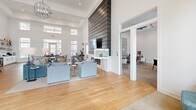 Located at 157 Hathaway Ln in Mooresville, NC, this single-floor community clubhouse offers a spacious, open-concept layout designed for both gathering and relaxation. The interior is defined by soaring ceilings with clerestory windows that flood the space with abundant natural light, complemented by crisp white walls and warm hardwood flooring throughout.

The main area is thoughtfully divided into distinct functional zones. A welcoming entry foyer greets visitors with large glass doors, transom windows, and a pair of teal accent chairs set atop a neutral area rug. Adjacent to the entry, a comfortable lounge area features plush gray sofas arranged around a dramatic floor-to-ceiling shiplap fireplace wall with a mounted flat-screen TV.

A dining and social area includes a long communal table with black spindle chairs, open shelving for refreshments, and a beverage refrigerator. A tufted banquette seating area with café-style tables sits beneath a striking large-scale geometric wall art piece, adding an artistic focal point to the room.

A separate windowed office or leasing space is accessible from the main floor, providing a semi-private area for meetings. The overall ambiance is clean, modern, and inviting, with a neutral palette, carefully curated furnishings, and an abundance of natural light creating a bright and welcoming community environment.