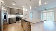 This thoughtfully designed 2-bedroom, 2-bathroom single-floor residence blends modern finishes with a warm, inviting ambiance throughout. The open-concept living area features light wood-style flooring, a ceiling fan, and large windows that flood the space with natural light and offer views of the surrounding outdoors. The living room flows seamlessly into the dining area, where a bright window serves as a backdrop, and into the kitchen, which is outfitted with granite countertops, wood-toned cabinetry with gold hardware, stainless steel appliances, a deep basin sink, and pendant lighting over the island — ideal for both cooking and entertaining. The primary bedroom is a comfortable retreat with plush carpeting, a ceiling fan, and a large window, complemented by a well-appointed en suite bathroom featuring a wood-tone vanity with granite countertops, backlit mirrors, and tile flooring. The second bedroom is equally inviting with carpeted floors, a ceiling fan, and generous natural light. A second full bathroom includes a tiled tub-shower combination and clean, neutral finishes. Two closets provide ample storage throughout the home.