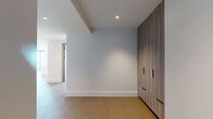 This contemporary residence in Denver, CO offers a thoughtfully designed single-floor layout with four bedrooms, two bathrooms, and three closets. The open-concept living and kitchen area is a standout, anchored by dramatic floor-to-ceiling windows that flood the space with natural light and frame expansive views of the Denver skyline and surrounding cityscape. Light-toned hardwood flooring flows seamlessly throughout, enhancing the bright, airy atmosphere.

The kitchen is a chef's showcase, featuring a large waterfall-edge island with an undermount sink and matte black fixtures, sleek two-tone cabinetry in warm wood and slate blue, and a professional-grade range — all complemented by a pendant light in brushed gold. A dedicated built-in cabinetry wall with a wine refrigerator adds a refined entertaining touch to the living area.

The bedrooms are generously proportioned, with the primary suite offering a private balcony accessible through sleek black-framed sliding glass doors. Bedrooms include ceiling fans and walk-in closets with custom wood shelving. Both bathrooms are elegantly finished with large-format marble-look tile, warm wood vanities, white countertops, and matte black hardware — one featuring a glass-enclosed walk-in shower, the other a soaking tub. A warmly lit corridor connects the private quarters with ease.