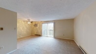 This single-floor residence offers a well-organized layout with a variety of functional spaces finished in warm, neutral tones throughout. The generously sized living room serves as the central gathering area, featuring plush wall-to-wall carpeting, a textured ceiling, a ceiling fan with an integrated wall-mounted air conditioning unit, and a baseboard heating system. A sliding glass door flanked by vertical blinds opens to a private balcony, allowing natural light to fill the room and providing outdoor views.

The kitchen is equipped with dark espresso cabinetry, granite-style countertops, stainless steel appliances including a refrigerator, dishwasher, and range, and durable wood-look flooring. Multiple bedrooms are carpeted and painted in soft warm tones, each featuring windows with blinds that bring in natural light and baseboard heaters for climate control. Textured ceilings are present in several rooms.

The full bathroom includes a tub-shower combination, a wood-vanity with a light countertop, and wood-look flooring. A separate half bathroom features a wall-mounted sink, an oval decorative mirror, and matching wood-look flooring, offering added convenience.