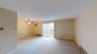 This single-floor residence offers a well-organized layout with a variety of functional spaces finished in warm, neutral tones throughout. The generously sized living room serves as the central gathering area, featuring plush wall-to-wall carpeting, a textured ceiling, a ceiling fan with an integrated wall-mounted air conditioning unit, and a baseboard heating system. A sliding glass door flanked by vertical blinds opens to a private balcony, allowing natural light to fill the room and providing outdoor views.

The kitchen is equipped with dark espresso cabinetry, granite-style countertops, stainless steel appliances including a refrigerator, dishwasher, and range, and durable wood-look flooring. Multiple bedrooms are carpeted and painted in soft warm tones, each featuring windows with blinds that bring in natural light and baseboard heaters for climate control. Textured ceilings are present in several rooms.

The full bathroom includes a tub-shower combination, a wood-vanity with a light countertop, and wood-look flooring. A separate half bathroom features a wall-mounted sink, an oval decorative mirror, and matching wood-look flooring, offering added convenience.