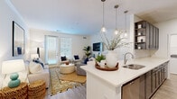 Located at 200 Big Wds Dr in Poquoson, Virginia, this well-appointed 2-bedroom, 2-bathroom residence offers a thoughtfully designed single-floor layout with clean, contemporary finishes throughout. The open-concept living and kitchen area serves as the heart of the home, where the kitchen stands out with sleek gray shaker-style cabinetry, white quartz countertops, stainless steel appliances, and glass pendant lighting over a spacious island with an undermount sink. Light wood-style flooring flows seamlessly into the bright living room, which features crown molding, abundant natural light from large windows and a glass exterior door, and a warm, inviting ambiance. Both bedrooms are carpeted and comfortably sized, with the primary bedroom offering ample closet space and natural light. The two bathrooms are finished with wood-look tile flooring, gray cabinetry, and white quartz countertops; one features a tub-shower combination, while the other includes a double vanity. A dedicated in-unit laundry room houses a full-size washer and dryer, adding everyday convenience. The overall design palette of soft whites, warm neutrals, and gray tones creates a cohesive, modern aesthetic throughout the home.