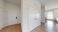 This contemporary single-floor residence showcases a clean, modern aesthetic defined by bright white walls, light wood-tone flooring, and an abundance of natural light throughout. The open-concept layout seamlessly connects the kitchen and living area, creating a spacious and functional common space. The kitchen is thoughtfully designed with two-tone cabinetry in white and dark gray, a marble-style granite countertop peninsula, a classic subway tile backsplash, and a full suite of stainless steel appliances including a side-by-side refrigerator, range, and microwave. Large windows with horizontal blinds frame city views and bathe the living area in natural light. The generous living space features recessed lighting and flows easily into the adjacent bedroom corridor. Bedrooms are well-proportioned, each featuring light hardwood-style flooring, large windows, and ample closet space, including a sliding-door closet with built-in shelving. The bathroom is finished with floor-to-ceiling white tile surrounding a soaking tub and shower, a granite-top vanity with white cabinetry, and polished chrome hardware. The entryway is anchored by a keypad-secured front door and a set of double doors providing generous storage. The space presents a cohesive, move-in-ready environment with a clean, contemporary character.