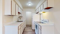 This single-floor residence offers a straightforward, functional layout designed to maximize use of space. The galley-style kitchen is efficiently organized with white cabinetry lining both walls, providing generous storage above and below the countertops. White appliances, including a refrigerator and electric range with overhead ventilation, are complemented by light countertops and wood-look flooring, creating a clean, practical workspace. A stainless steel sink with a brushed nickel faucet adds a modern touch.

The living area is carpeted and receives natural light through a large sliding glass door that opens onto a balcony overlooking a wooded outdoor setting. An additional side window fitted with vertical blinds further brightens the space. The bedrooms are also carpeted and feature standard closets with bifold doors, offering practical storage solutions. One bedroom includes a window with views of surrounding trees.

The bathroom is finished with small-format mosaic tile flooring, a white vanity with an integrated sink, a mirrored medicine cabinet, and a full-size tub enclosed by white square ceramic wall tiles. The overall palette throughout the residence is neutral and light, contributing to a clean, cohesive ambiance.