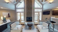 Located in Kent, Washington, this single-story community clubhouse at 11101 SE 208th St offers a well-appointed gathering and amenity space designed for both comfort and function. The centerpiece of the building is a grand lounge area distinguished by soaring vaulted ceilings, dramatic floor-to-ceiling windows arranged in a gabled formation, and an impressive floor-to-ceiling mosaic tile fireplace that anchors the room. Natural light floods the space through the expansive glazing, while views of the outdoor pool area are visible through glass-paneled doors on either side. Modern white lounge seating and a circular ottoman complete the inviting atmosphere. Adjacent to the lounge, a carpeted reception and common area features recessed lighting, a wall-mounted TV, and a service counter, providing a welcoming entry experience. The leasing office offers a refined workspace with vaulted ceilings, a ceiling fan, large transom windows, and an elegant dual-workstation desk. The fitness center is comprehensively equipped with treadmills, ellipticals, a multi-station cable machine, free weights, kettle bells, stability balls, resistance bands, and wall-to-wall mirrors, all beneath vaulted ceilings with windows overlooking the pool courtyard. Together, these spaces create a polished and functional community hub.